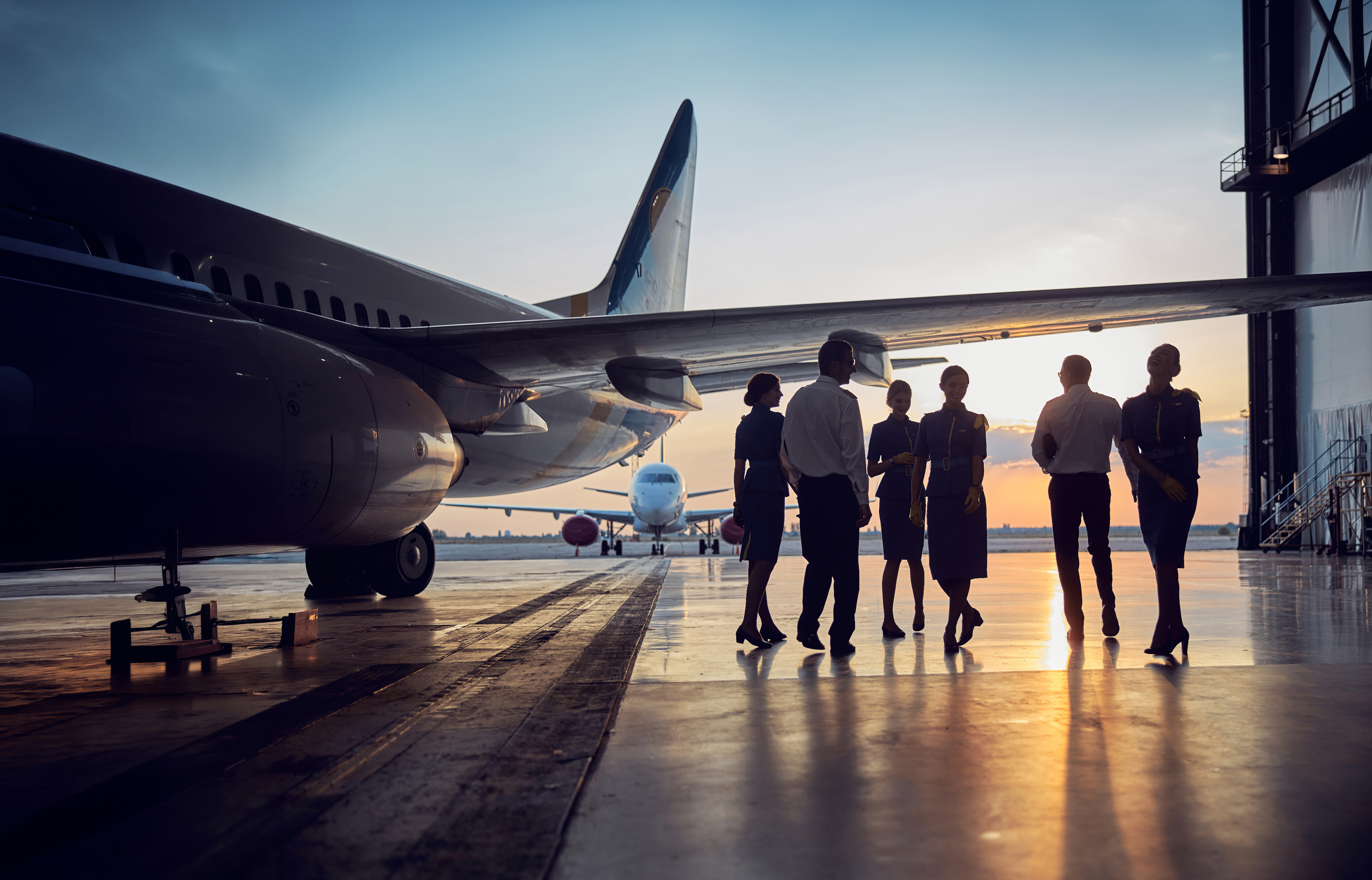 Aviation crew walking beside aircraft in a hangar at sunset