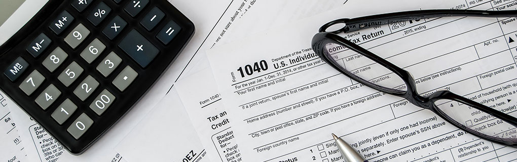 Tax Return Forms with Calculator, Pen and Eye Glasses on Table - Lead Image for Tax Services Page