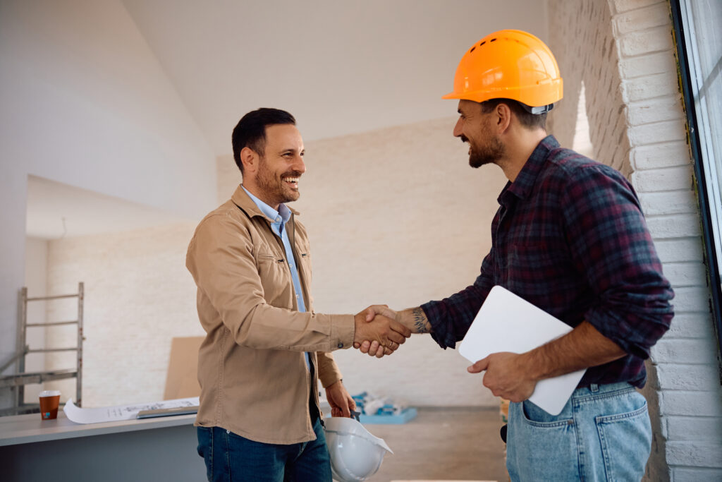 Contractor and project owner shaking hands at a construction site, symbolizing trust and agreement through contract bonds.