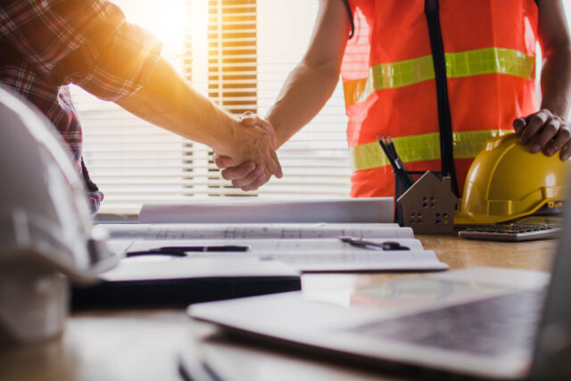 Contractor shaking hands with a client at a construction site, symbolizing trust and agreement in project completion.